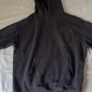 Svart hoodie Pull&Bear med tryck bak och fram. Storlek S - Svart hoodie från Pull&Bear med stor blom- och textprint både fram och bak. Klassisk känguruficka, huva och relaxed fit. Snyggt tryck med blommor och texten 'Capax Infinit'. Perfekt för dig som gillar streetstyle och vill ha en hoodie med unik design.