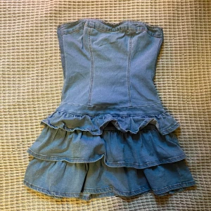 Jeansklänning - Jättesnygg bandeau klänning i stretchiga jeansmaterial. Volang nedtill och tight upptill! Utsydd vid bysten men det går att ta bort och sy igen igen ifall det skulle önskas! Saknar lapp så vet ej märket, men den är köpt secondhand men aldrig använd! Står ingen storlek men uppskattar M kanske L så materialet är stretchigt!!!💗💗