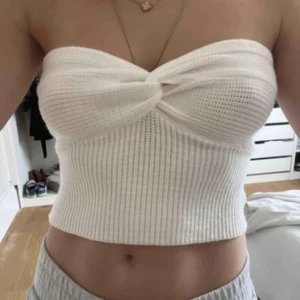 Vit ribbad bandeau tubtopp - Supersnygg vit bandeau tubtopp med twistad detalj framtill. Toppen är ribbstickad och sitter tight över kroppen, perfekt för att skapa en clean och trendig look. Mjuk och stretchig, passar till många olika outfits.
