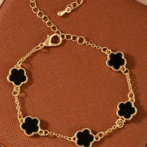 Guldarmband med svarta blommor - Snyggt armband i guldfärgad metall med fem svarta blommor som detaljer. Kedjan är tunn och har justerbar längd med karbinlås. Blommorna har en mjuk, rundad form och ger en cool kontrast mot det guldiga. Perfekt för dig som gillar stilrena och trendiga accessoarer.