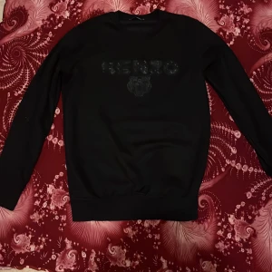 Svart Kenzo sweatshirt med logga - Svart sweatshirt från Kenzo med klassisk rund hals och broderad Kenzo-logga samt tiger på bröstet. Tröjan har lång ärm och en stilren, enkel design som passar perfekt till jeans eller kjol. Materialet känns mjukt och bekvämt mot huden.
