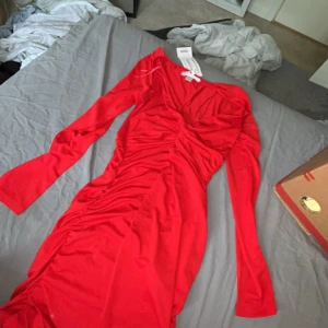 Röd långärmad klänning från MISU - Snygg röd klänning från MISU i storlek 38. Klänningen har långa ärmar, figurnära passform och snygga rynkade detaljer längs sidorna. Tillverkad i ett mjukt och stretchigt material som sitter bekvämt. Perfekt för dig som vill sticka ut med en färgstark look.