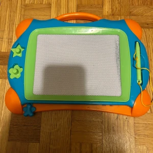 Magnetisk ritplatta - En färgglad magnetisk ritplatta med medföljande penna och stämplar i form av stjärna och blomma. Perfekt för att skapa egna konstverk, skissa eller skriva meddelanden. Enkel att använda och passar både för kreativa stunder och avslappnad underhållning.