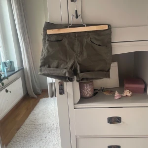 Olivgröna shorts från H&M Divided - Snygga olivgröna shorts från H&M Divided i storlek 36. Modellen har klassisk femficksdesign, uppvikta benslut och knapp- samt dragkedja framtill. Materialet är mjuk bomull med lite stretch för skön passform. Perfekta för varma dagar och chill häng.