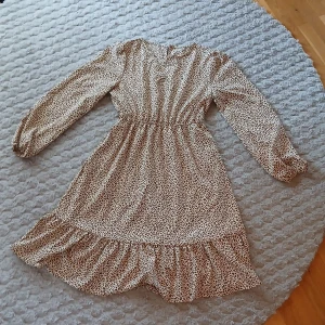 Leopardmönstrad kortklänning med volang - Säljer en beige kortklänning med brunt leopardmönster och volang nertill. Klänningen har långärmade puffärmar med resår vid handlederna och markerad midja med resår. Materialet känns lätt och flowy, perfekt för dig som gillar djurmönster och vill sticka ut.