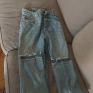 Ljusblå jeans från boohooMAN med slitningar - Säljer ett par ljusblå jeans från boohooMAN med råa slitningar över knäna och fransade benslut. Jeansen har klassisk femficksdesign och raka ben. Perfekta för en avslappnad streetstil och passar till sneakers eller boots.