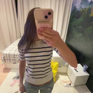 Randig vit tröja från Zara - Vit tröja från Zara med marinblå horisontella ränder. Modellen har korta ärmar och rund halsringning. Tröjan är i mjuk bomull och har en klassisk, lite tight passform som sitter snyggt till jeans eller kjol. Knappt använd i bra skick💕💕