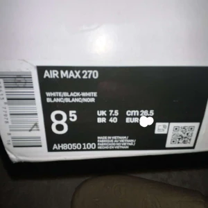 Nike Air Max 270 svart/vit sneakers - Nike Air Max 270 sneakers i svart och vitt med tydlig Air Max-dämpning i hälen. Ovandel i mesh för bra andningsförmåga, vit sula med orange och svarta detaljer undertill. Snygg och sportig look med klassisk Nike-logga på sidan.