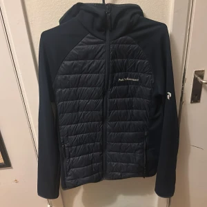 Mörbklå Cardigain Peak Performance M - Snygg mörkblå cardigain/pufferjacka från Peak Performance med quiltad framsida och huva. Jackan har dragkedja hela vägen, två fickor och diskret logga på bröstet. Perfekt för kyliga dagar och har en sportig vibe. Materialet är polyester och syntet. Perfekt nu till hösten, pris kan diskuteras men inga flyballs tack!