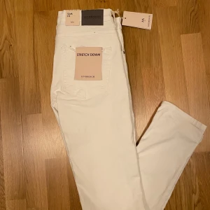Vita stretchjeans från Lindbergh - Snygga vita jeans från Lindbergh med slim fit och stretchigt denimtyg. Klassisk femficksmodell med silverfärgade nitar och knapp, samt diskret logga på fickan. Perfekta för dig som gillar stilrena och fräscha byxor med smal passform. Helt oanvända.