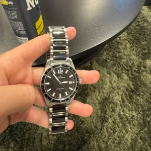 Jacques Lemans Cemaric Sport 100 - Stilren klocka från Jacques Lemans ceramic sport 100 med svart urtavla, datumvisning och tydliga index. Armbandet är i silverfärgat rostfritt stål med svarta keramiska länkar. Sportig design med markerad bezel och klassisk låsning. Perfekt accessoar för dig som gillar en clean look. Prisej ej fast 👍