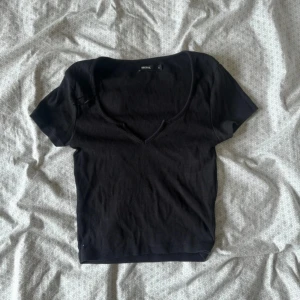 Svart ribbad topp med v-ringning Bik Bok - Svart ribbad topp från Bik Bok med snygg v-ringning och korta ärmar. Modellen är croppad och sitter tajt mot kroppen. Tillverkad i ekologisk bomull och elastan för en skön stretchig känsla. Perfekt till jeans eller kjol för en enkel men stilren look.