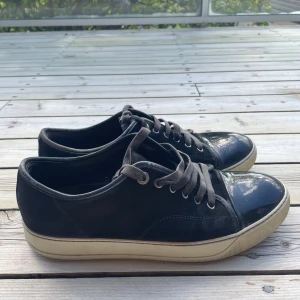 Svarta sneakers från Lanvin med lackad tå - Snygga mörkblå sneakers från Lanvin med klassisk låg profil, snörning och vit slula. Ovandelen är i mocka och tån är i blankt lackskinn. Perfekta för dig som gillar stilrena men unika detaljer.