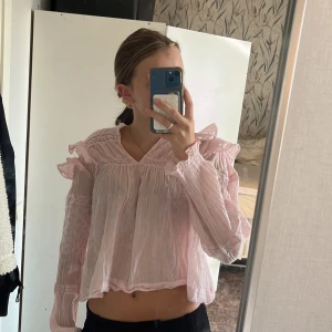Ljusrosa volangblus med v-ringning - Supersöt ljusrosa blus med volangdetaljer på axlar och ärmar från Gina i storlek 170. Blusen har v-ringning, långärmad design och är tillverkad i ett tunt, luftigt tyg med lätt struktur. Perfekt för dig som gillar romantisk och feminin stil.