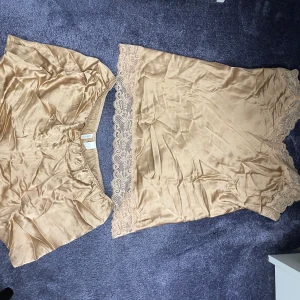 Champagnefärgad pyjamas Intimissimi - Säljer en champagnefärgad pyjamas från Intimissimi i mjuk satin med tunna axelband och vacker spetskant längs nederdelen. Materialet känns lyxigt, luftigt och har fin glans.