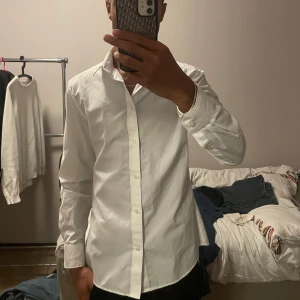 Vit slim fit skjorta från H&M - Klassisk vit skjorta från H&M i slim fit-modell. Skjortan har långa ärmar, knappar framtill och är tillverkad i ett lätt och bekvämt bomullstyg. Perfekt för dig som gillar en stilren och clean look.