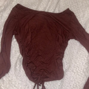 Brun ribbad offshoulder topp - Snygg brun ribbad topp med offshoulder och långa ärmar. Sidorna har trendig snörning som ger en cool rynkad effekt och gör att du kan justera passformen. Perfekt för dig som gillar en stilren men ändå unik look.