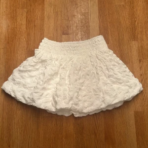 Vit kortkjol från Kappahl - Supersöt vit kortkjol från Kappahl med volangig och krinklad struktur. Kjolen har bred resår i midjan som gör den bekväm och enkel att ta på. ❤️