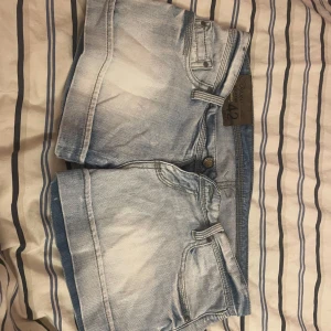 Ljusblå jeansshorts low waist  - Snygga ljusblå jeansshorts som är lågmidjade med klassisk femficksdesign och coola broderade detaljer på bakfickorna. Shortsens material är slitstarkt denim och de har uppvikta benslut samt knapp och dragkedja framtill. Perfekta för varma dagar och chill stil. Storlek M
