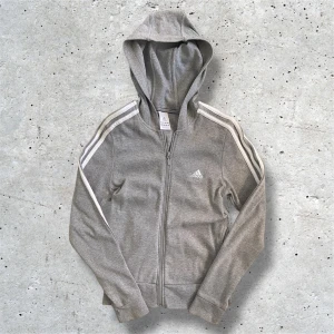 Grå Adidas hoodie - Grå Adidas hoodie i storlek 36 eller 38 i dam vilket motsvarar S. Hoodien har inga defekter förutom att den är lite urtvättad som man märken lite på materialet. Hör av er vid frågor, pris kan diskuteras!