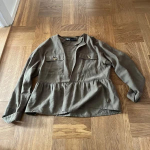Olivgrön overshirt från Zara - Säljer en olivgrön overshirt från Zara med två stora bröstfickor med knappar och snygg volang nedtill. 