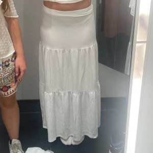 Vit långkjol med volanger från Gina Tricot  - Säljer en vit långkjol med snygga volangdetaljer. Kjolen har en hög midja och är tillverkad i ett lätt och luftigt bomullstyg som ger en skön känsla. Perfekt för dig som gillar en enkel men trendig look med lite boho-vibe. Skriv för fler bilder eller frågor❤️