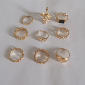 Set med 9 guldiga ringar i olika former - Säljer ett set med 9 snygga guldiga ringar i olika former och detaljer. Bland annat en cool ormring. Perfekt för dig som gillar att mixa och matcha flera ringar på samma hand. Materialet är alloy. (123)
