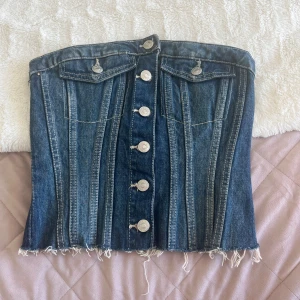 Jeans korsett-topp med knappar - Snygg korsett-topp i mörkblå denim med silverfärgade knappar framtill. Den är i nyskick använd 1 gång. 