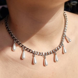 Silverhalsband med droppformade pärlor - Stilrent halsband i silverfärgad metall med chunky kedja och sju droppformade vita pärlor som hänger längs hela halsbandet. Perfekt statement piece för dig som gillar att sticka ut och addera lite edge till din look.