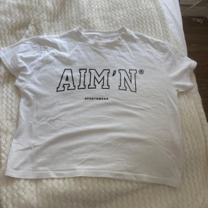 Vit AIM'N t-shirt med tryck - Vit t-shirt från AIM'N med svart tryck framtill. Klassisk rund hals och korta ärmar. Tillverkad i mjuk bomull som känns skön mot huden. Perfekt för en sportig och avslappnad stil. Säljer då den aldrig kommer till användning 