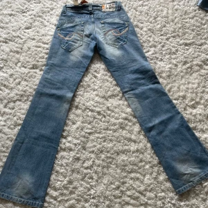 Blå bootcut jeans från G-Lago - AS snygga lågmidjade ljusblå bootcut jeans från G-Lago med slitningar och broderade detaljer på bakfickorna. Tyvärr för små så be inte om bild på. Andra bilden visar jeansens mått. Aldrig använda. 💗