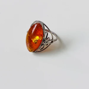 Vintage ring med stor orange bärnsten - Unik ring  med en stor, oval orange bärnsten som har glittrande inslag. Ringen har detaljerade, blommiga dekorationer på sidorna och en snygg vintagekänsla. Perfekt för dig som vill sticka ut med ett statement-smycke.