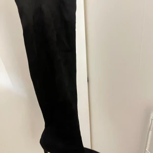 Svarta höga stövlar med klack - Snygga svarta overknee-stövlar i mocka-look med spetsig tå och hög smal klack. Perfekta för att lyfta din outfit med en elegant och edgy vibe. Stövlarna har en stilren design och passar dig som gillar att sticka ut. Storlek 39