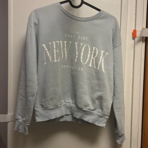 Ljusblå sweatshirt från Kappahl - Snygg ljusblå sweatshirt från Kappahl med stort vitt tryck 'NEW YORK' på framsidan. Tröjan har rund hals, ribbade muddar och är långärmad. Perfekt för dig som gillar streetstyle och vill ha en chill vibe.