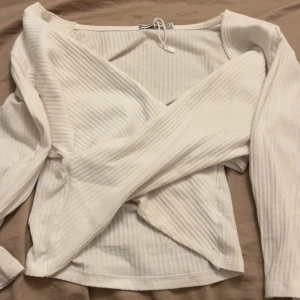 Vit omlottopp från Stradivarius - Superfin vit omlottopp från Stradivarius i ribbad bomull. Toppen har lång ärm, v-ringning. Perfekt för dig som gillar en clean och stilren look med en twist. Snygg att matcha med både jeans och kjol.
