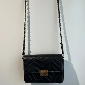 Svart quiltad axelväska med kedja - Snygg svart axelväska i quiltat skinnimitation med guldiga detaljer och kedjerem. Har anvönds en del men är i väldigt gott skick💞