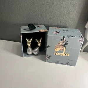 Guldörhängen med pärlor från Ioaku - INTRESSEKOLL på detta eleganta örhängen från Ioaku i guld med stora vita pärlor. Köpte dessa när jag var i Stockholm men fick aldrig användning för dem. Designen har en unik form med detaljer som liknar kaninöron. Perfekta för att ge en lyxig touch till din stil.