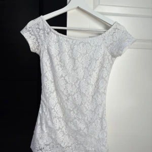 Vit spets topp - Superfin vit topp i spets med offshoulder och korta ärmar. Blusen har ett blommönster i spets.