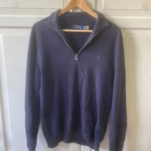 Marinblå stickad tröja Polo Ralph Lauren - Snygg marinblå stickad tröja från Polo Ralph Lauren med half zip och lång ärm. Mycket bra skick men litet hål på ryggen. Storlek S. Hör av er vid intresse!!