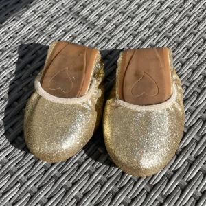 Ihopvikbara Glittriga guldiga ballerinaskor - Snygga ballerinaskor i guld med glittrig yta och rund tå. Skorna har elastisk kant för skön passform. Perfekt att som extraskor i väskan!