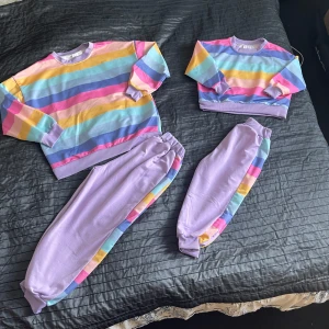 Matchande kläder  - Matchande kläder.Superfin sweatshirt med breda pastellfärgade ränder i rosa, blått, lila, gult och mint. Tröjan har ribbade muddar och rund hals, tillverkad i mjuk bomull. Perfekt för dig som gillar färgglada och chill vibes. Matcha med lila mjukisbyxor med randiga detaljer på sidan.Två set.Storlek passar  128 och 92
