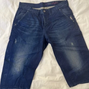 Mörkblå jeansshorts från edc - Snygga mörkblå jeansshorts från edc med klassisk femficksdesign och slitna detaljer framtill. Shortsen har normal passform och är tillverkade i jeansmaterial med en knapp och dragkedja i midjan. Perfekta för en avslappnad stil under sommaren.
