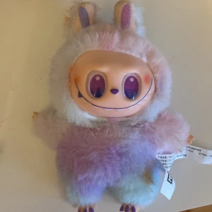 Labubu/lafufu - Bilderna visar en färgglad och fluffig Pop Mart-leksak med stora glittriga ögon och ett brett leende. Den har pastellfärgad päls och söta öron, perfekt som samlarfigur eller dekoration för dig som gillar unika och trendiga prylar. Passar både ungdomar och unga vuxna som vill ha något annorlunda. Ej använd,jag står inte för om packet försvinner i frakten 200 kr + frakt