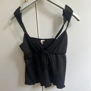 Svart linnetopp från Nelly XS - Helt o använd.Svart linnetopp från Nelly i storlek XS. Toppen har breda axelband, knytning framtill och lätt rynkad struktur. 