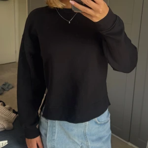 Svart sweatshirt med slits i sidan - Svart sweatshirt med rund hals och lång ärm, tillverkad i mjuk bomull. Tröjan har en loose passform och cool slitsdetalj på sidorna. 