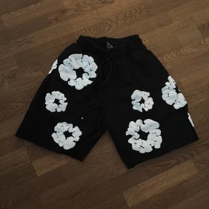 Denim tears shorts - Svarta shorts med coola vita blommönster över hela tyget. De har en loose passform och elastisk midja med snörning för extra komfort. Perfekta för sommarens chill dagar och har en unik streetwear vibe. ⚠️1:1⚠️