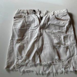 Vit jeanskjol från DIVIDED, strl 34 - Säljer en vit kort jeanskjol från DIVIDED i storlek 34. Kjolen har slitna detaljer, fransad nederkant och klassiska fickor fram. Stängs med dragkedja och knapp. Perfekt för dig som gillar en edgy och avslappnad stil.