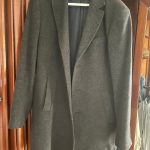 Mörkgrå ullkavaj från Sand - Snygg mörkgrå kavaj från Sand i ull med klassisk passform. Fodret har ett diskret blommigt mönster och kavajen har tre knappar vid ärmslutet. Perfekt för dig som gillar stilrena och tidlösa plagg med lite extra detaljer.