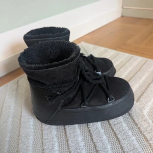 Svarta Inuikii moon boots i mocka och skinn - Köpta på Vinted, jag har inte använt de, säljs då det inte var den modellen jag ville ha. Beskrivningen finns på sista bilden, sulan är lite nedtrampad.                                                                                    Ett par svarta Inuikii boots med mjuk insida och snörning runt hela skon. Utsidan är i mocka och skinn, med en rund tå och platt sula. Perfekta för kalla dagar med sin fluffiga och varma känsla. Snygg, chunky look som sticker ut.