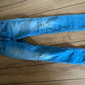 Replay ljusblå  jeans med slitningar - Säljer ett par ljusblå skinny jeans från Replay med snygga slitningar på låret och knät. Jeansen har klassisk femficksdesign, dragkedja och knapp framtill  och en avslappnad streetstil. 